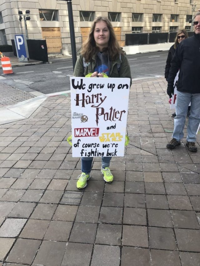 Photo of a teenager holding a protest sign which reads: We grew up on Harry Potter, the Hunger Games, Marvel and Star Wars. Of course w'ere fighting back.